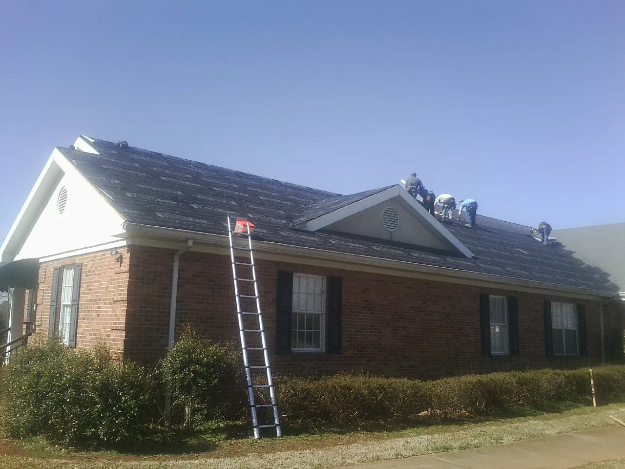 Crew tearing shingles off a brick ranch roof with a ladder set — Metal Roof Repair work by our crew in Hickory Valley