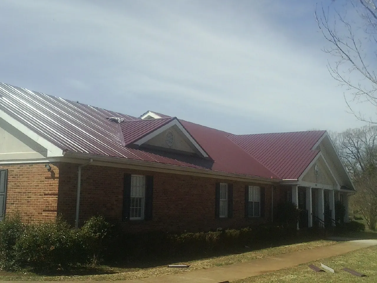 Red metal roof with gabled entries on a long brick building, from a Hail Damage Roof Repair job in Hickory Valley