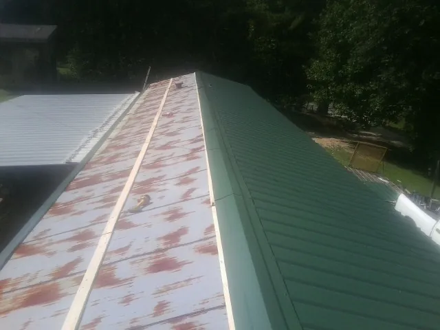Old rusted panels beside newly installed green metal roofing — Wind Damage Roof Repair by Roofing Brothers in Hickory Valley