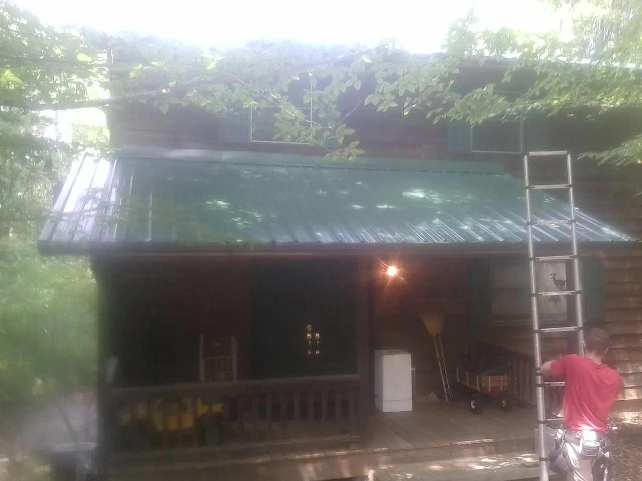 Worker on a ladder at the green porch roof of a wooded cabin in Hickory Valley