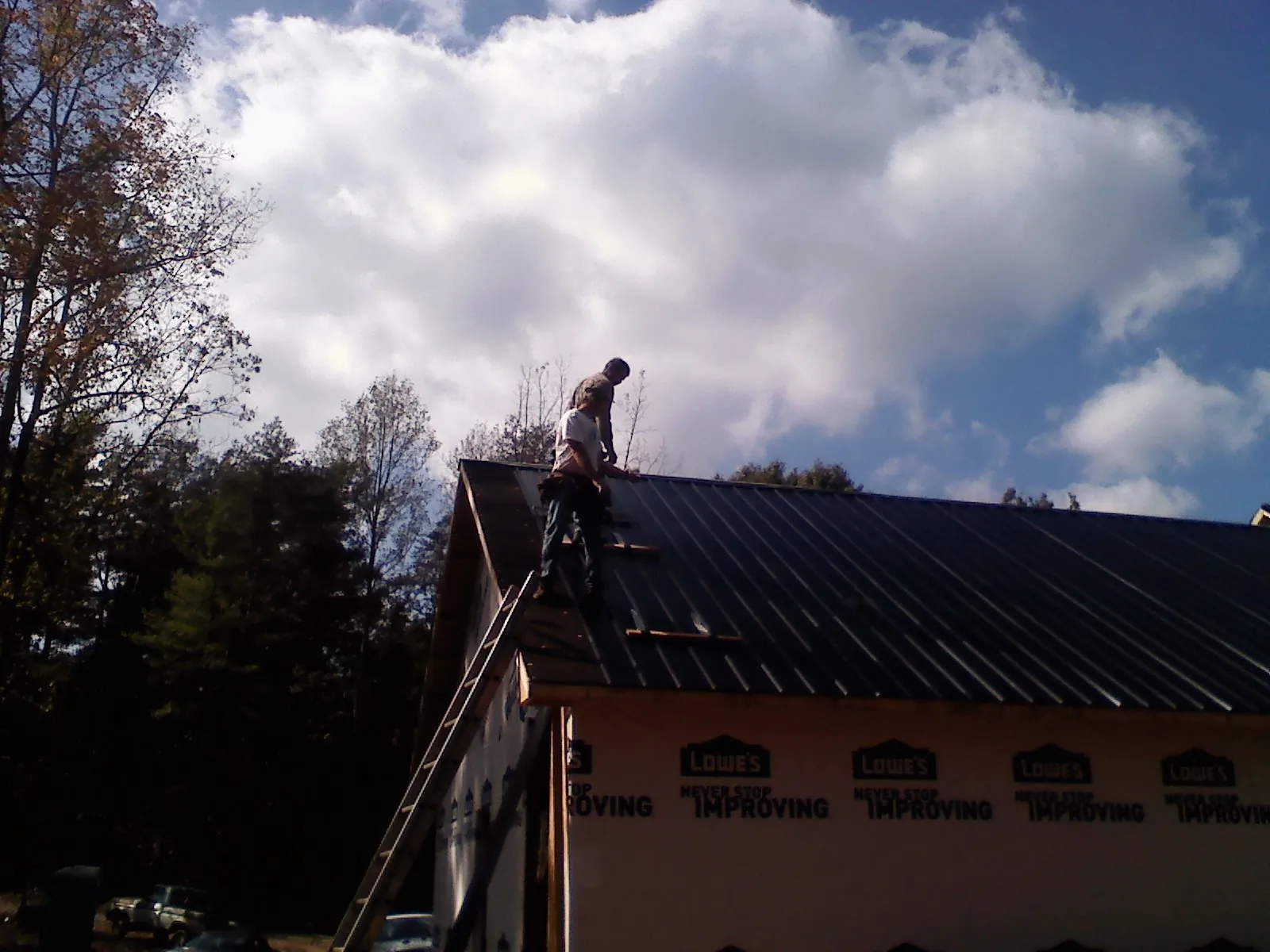 Roofer fastening dark metal panels high against a cloudy sky, from a Roof Inspection job in Hickory Valley