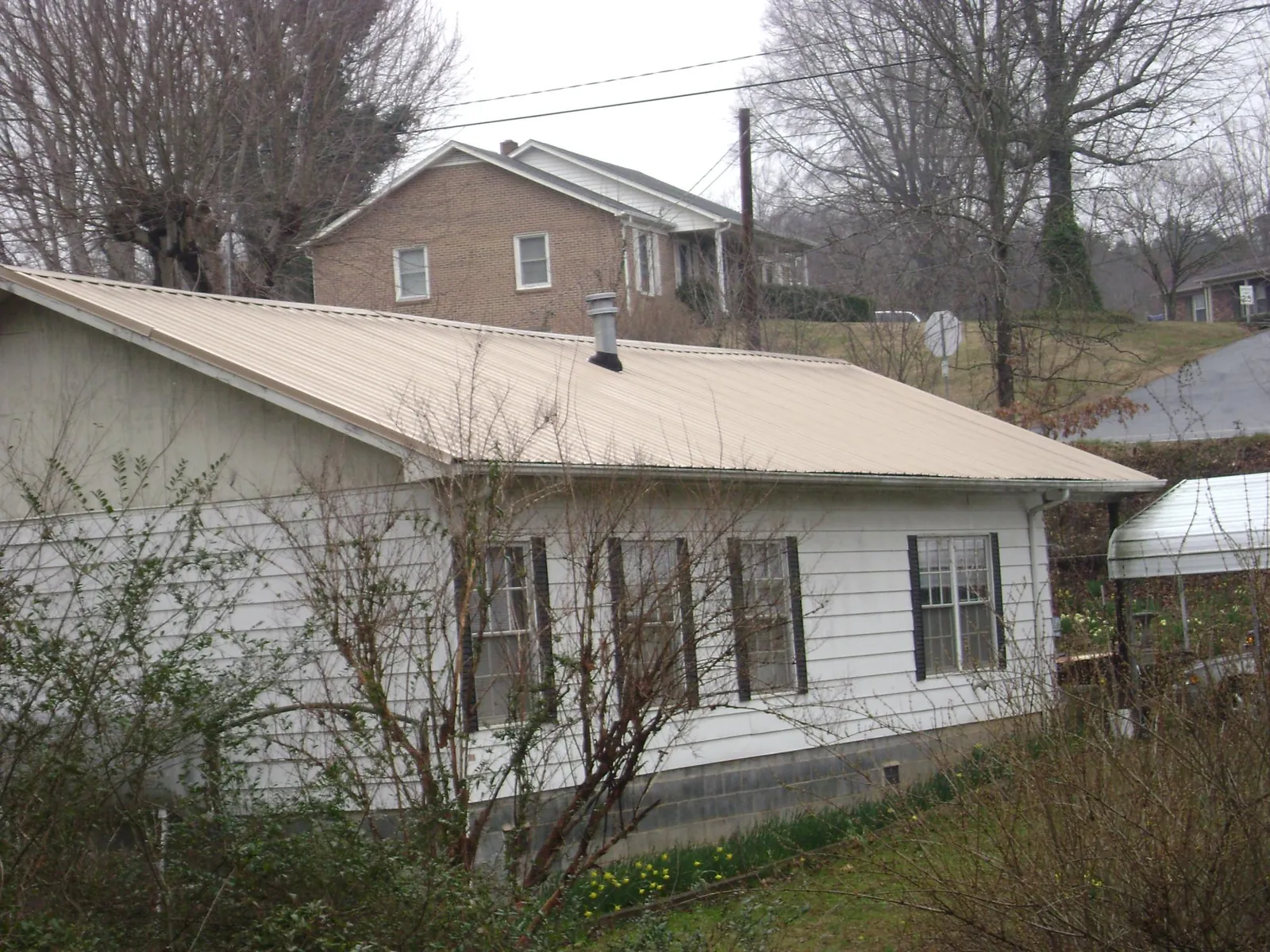 Tan metal roof on a white sided house set into a hillside — Commercial Roofing by Roofing Brothers in Hickory Valley
