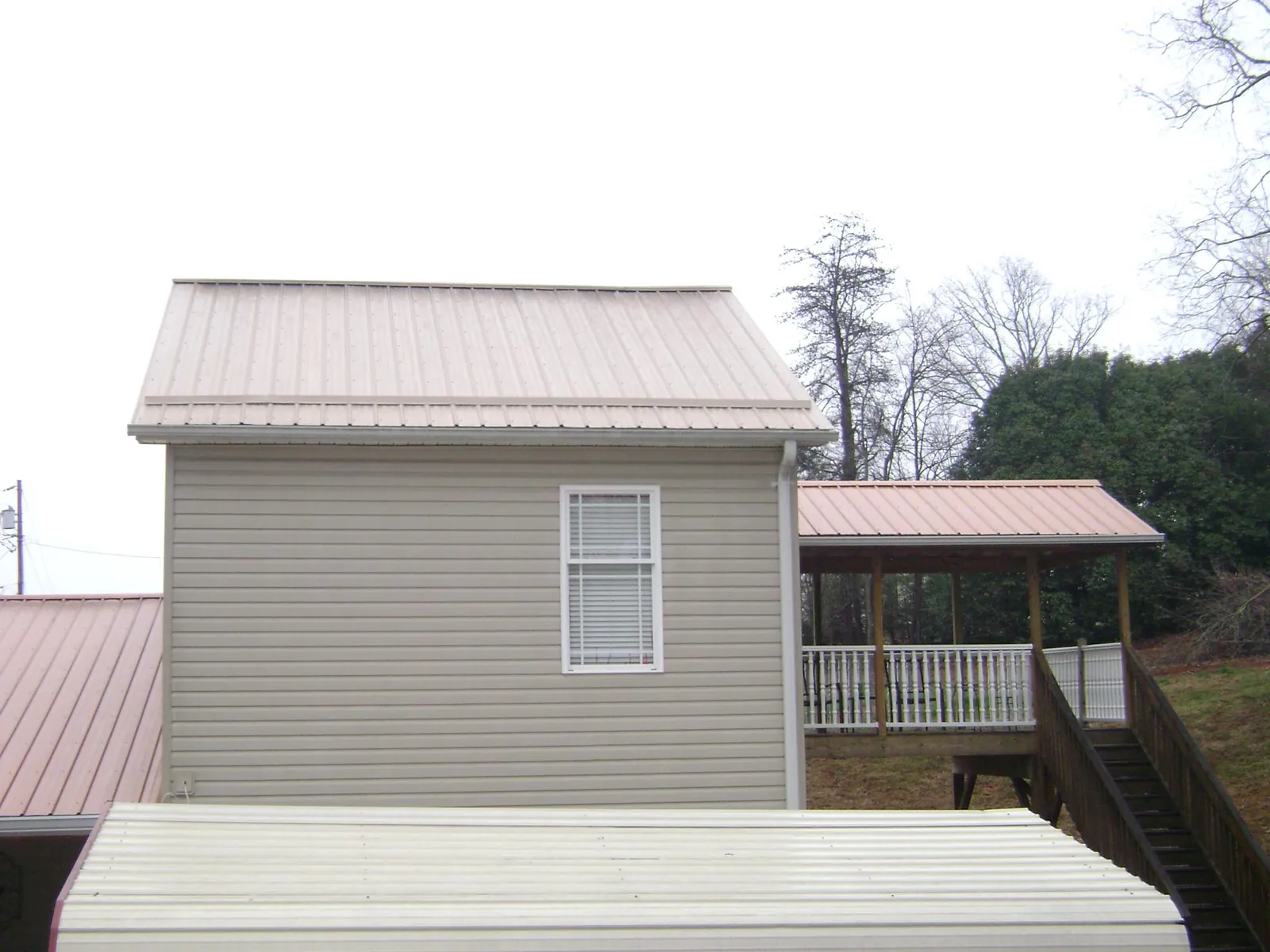 Tan metal roofs on a two story addition and attached porch, from a Roof Replacement job in Hickory Valley